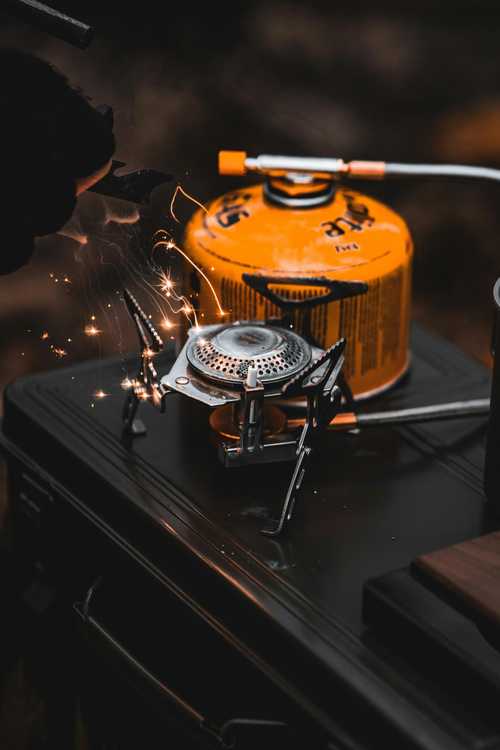 Close-up of a portable camping stove igniting with visible sparks, outdoors setting.